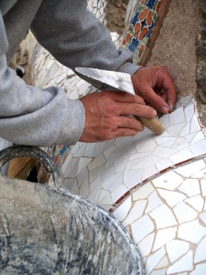 Hands and trowel cementing mosaic tiles in place